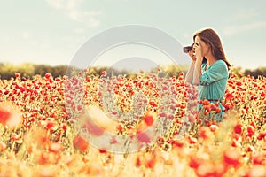 Girl taking photographs with camera in flower meadow.