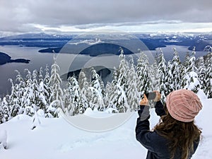 A girl taking a picture atop Cypress Mountain overlooking the ocean below.