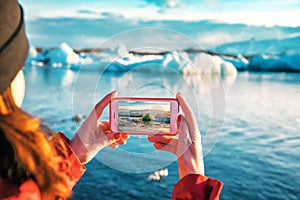 Girl taking a picture of a blue iceberg in Iceland