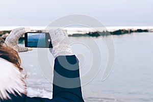 Girl taking pictures of the beach on a mobile phone in winter