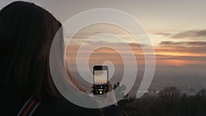 Girl taking pictures of beautiful sunset with her smartphone. Travel technology concept