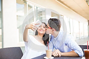 Girl Taking Selfie While Boyfriend Kissing On Cheek In Mall