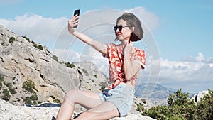 Girl taking a selfie on her phone against a background of mountains