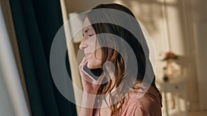 Girl talking mobile phone coming to window closeup. Smiling woman in sunlight