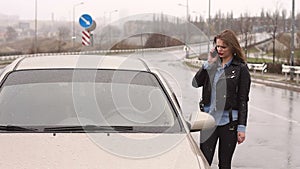 Girl talking on the phone near a broken car on the road in the rain.