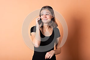 The girl is talking on the phone in surprise, on a light orange background