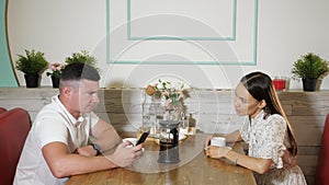 Girl talks with guy using smartphone at table in cozy cafe