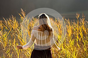 Girl with tattoo mountains on the shoulder standing and meditating in field of reeds / Blond girl walking through field of reeds