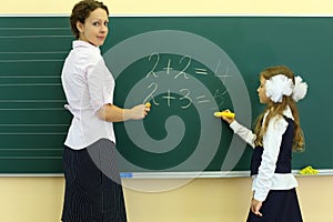 Girl and teacher stand near chalkboard and solve photo