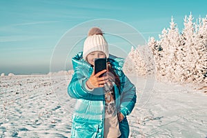 Girl teenager makes selfie on the background of a snowy forest on a sunny day