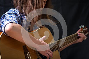 Girl teenager playing an acoustic guitar on a dark background in the Studio. Concert young musicians