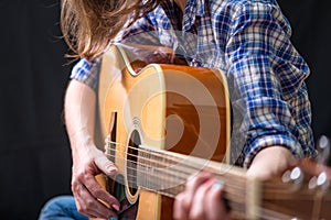 Girl teenager playing an acoustic guitar on a dark background in the Studio. Concert young musicians