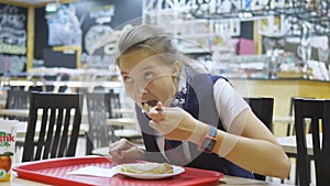 Girl teenager in a school uniform sitting at a table in the school cafeteria and eating.