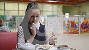 Girl teenager in a school uniform sitting at a table in the school cafeteria eating cakes and drinking tea.