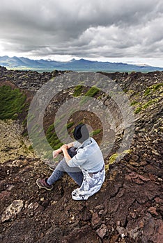 Girl teenager is sitting in the border of Eldborg volcano crater photo
