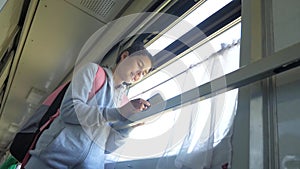 Girl teenager traveler with backpack stands lifestyle by the window of the train car with a smartphone. travel