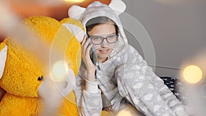 Girl teenager warm pajamas talking on a cell phone with a friend at the Christmas holidays.