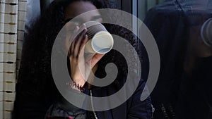 Girl teenager young woman teen wearing a black jacket sitting looking out of a window and drinking cup of coffee