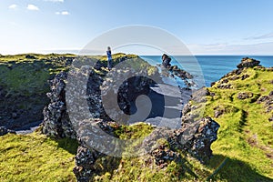 Girl Teenagers staying in the top of the lava rock observing the landscape of Djupalonssandur beach in Icelandic Snaefellsjokull