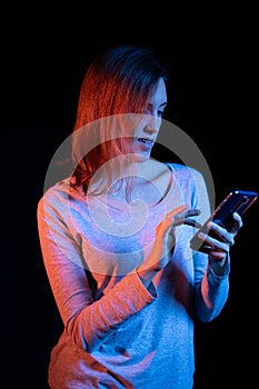 A girl texting in her smartphone, black background, blue and red light