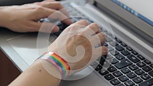 The girl is texting on a laptop, and on her hand is a bracelet with LGBTQI symbols.