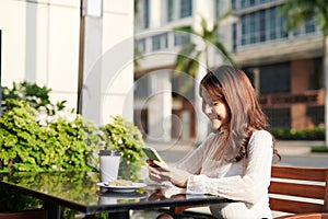 Girl texting on the smart phone in a restaurant terrace with an unfocused background