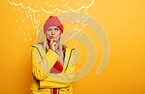 Girl thinks about negative things. Cloud, rain and lightning above her. Confused and pensive expression. Yellow