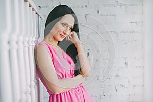 Girl thoughtfully looking down. Beautiful woman model in pink dress against a white brick wall