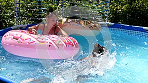 Girl throw down kid from donut float on sunny summer day, pool games