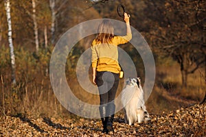 Girl throws black puller to Rough Collie in yellow autumn park