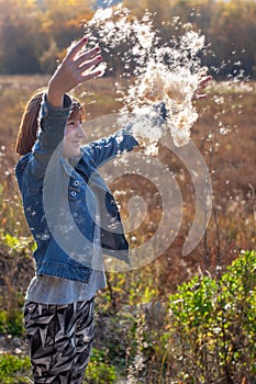 Girl throws fluff from cattail up in the sunshine on a fall day.