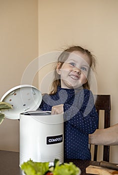 Girl throws vegetable peels into a compost bin. Dad cooks a vegetarian lunch with his daughter