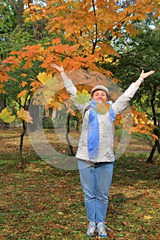 A girl throws yellow leaves into the air in an autumn park