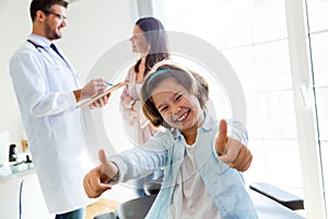 Girl with thumbs up while the doctor talks to her mother in the office.