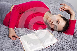 Girl is tired of reading book lying on bed. Attractive young brunette woman lies on bed with book in bedroom