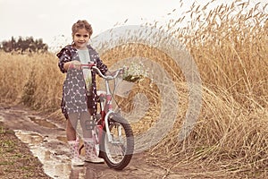 Girl to stand in the field with bicycle