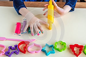 Girl toddler hands playing colorful play dough with plastic molds and yellow rolling pin