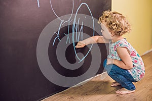 Girl toddler paint with chalk on a blackboard