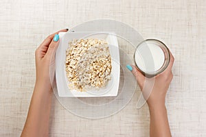 The girl took milk to pour it into oatmeal. Useful and healthy breakfast. light background