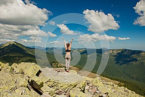 The girl at the top of the mountain raised her hands up. Wide summer mountain view at sunrise and distant mountain range covered.