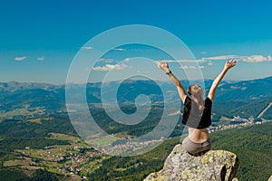 The girl at the top of the mountain raised her hands up. Wide summer mountain view at sunrise and distant mountain range covered.