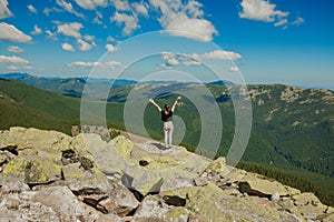 The girl at the top of the mountain raised her hands up. Wide summer mountain view at sunrise and distant mountain range covered.