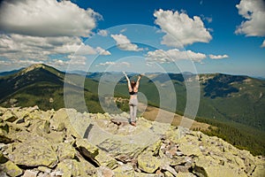 The girl at the top of the mountain raised her hands up. Wide summer mountain view at sunrise and distant mountain range covered.