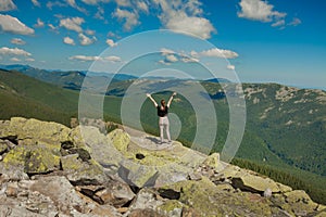 The girl at the top of the mountain raised her hands up. Wide summer mountain view at sunrise and distant mountain range covered.