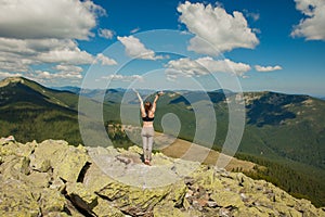 The girl at the top of the mountain raised her hands up. Wide summer mountain view at sunrise and distant mountain range covered.