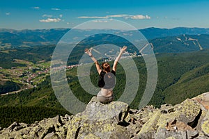 The girl at the top of the mountain raised her hands up. Wide summer mountain view at sunrise and distant mountain range covered.