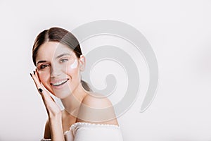 Girl touches moisturized skin and smiles. Portrait of model with cream on face on  background.