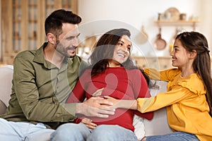 Girl Touching Mom& x27;s Pregnant Belly Sitting With Dad At Home