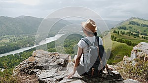Girl tourist with backpack sits on the top of rock with picturesque view