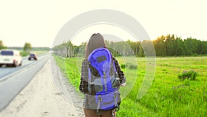 Girl tourist with backpack walking along the road, hitchhiking trip